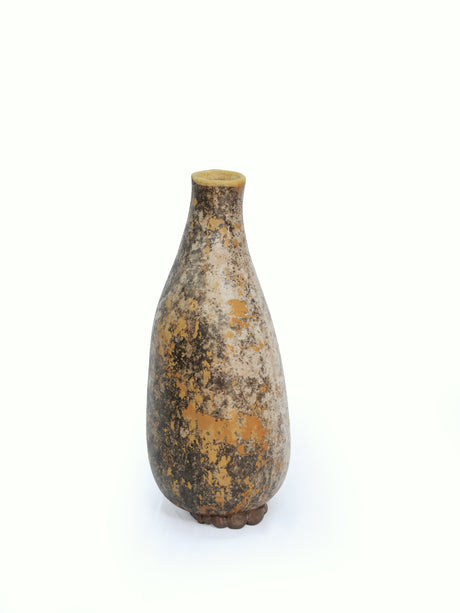A tall gourd vase with a narrow neck and long body, featuring a mottled texture in earthy brown, beige, and ochre tones, set against a plain white background.